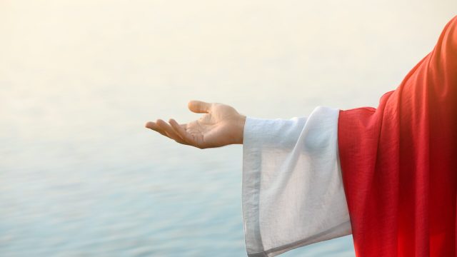 Jesus Christ reaching out his hand near water outdoors, closeup